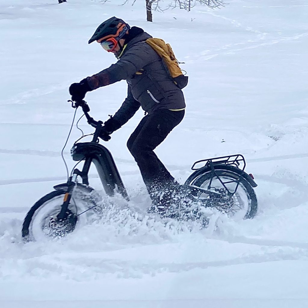 Matkariietus. Matkavarustus. Elektritõukerattamatk talvel. Tõukerattur sõidab lume näitab mis riietus on seljas