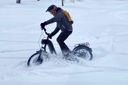 Matkariietus. Matkavarustus. Elektritõukerattamatk talvel. Tõukerattur sõidab lume näitab mis riietus on seljas